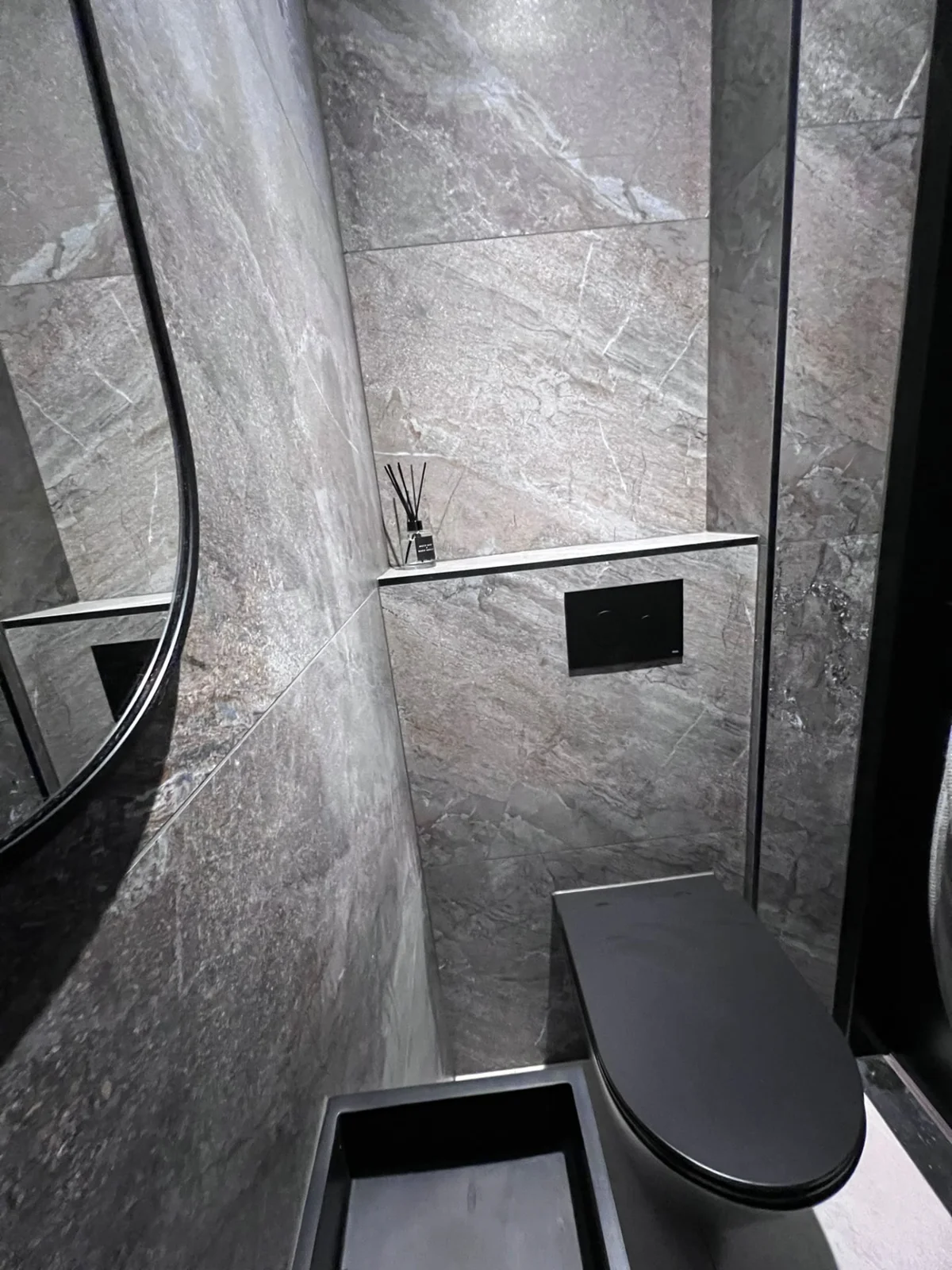 Hangend zwart toilet met grijze wandtegels en zwarte bedieningsplaat
