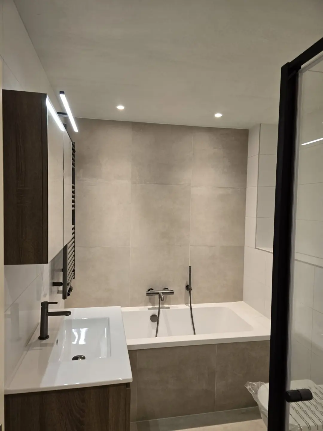 Ligbad met betonlook wand en spiegelkast — badkamerrenovatie in Nijmegen