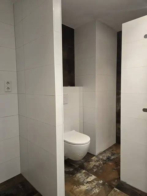 Toiletruimte met witte tegels en roestlook vloer — toiletrenovatie in Nijmegen